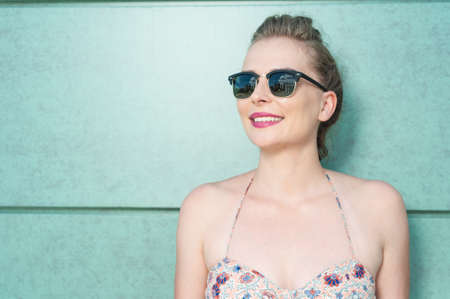 Beautiful woman wearing shades standing and being happy in summer outfit on green wall background with copy text spaceの写真素材