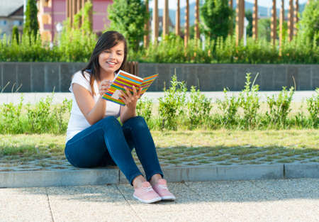 Pretty girl sitting down in park and reading from notebook or diary with copy text spaceの写真素材