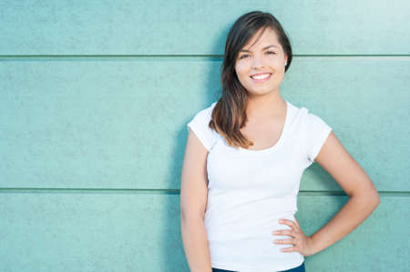 Portrait of beautiful girl smiling with hand on waist outside on green wall with copy text space