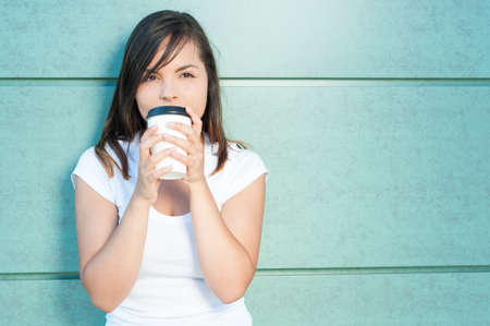 Girl sipping fresh coffee and being dreamy outside on green wall background with copy text areaの写真素材