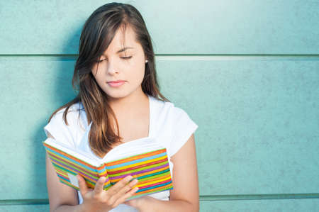 Beautiful girl reading from colorful agenda or diary on green wall background with copy space areaの写真素材
