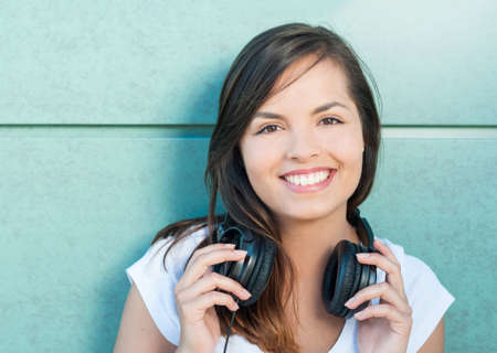Beautiful girl smiling and holding her headphones on green wall background with copy text spaceの写真素材