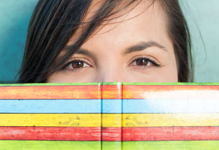 Close-up of attractive girl hiding behind colorful agenda or notebookの写真素材