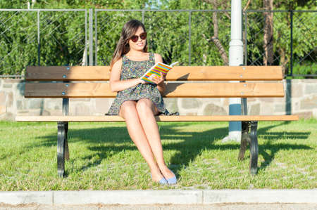Pretty lady sitting on bench outside in park and reading from agenda book or diary with copy text spaceの写真素材