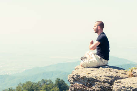 Young man meditating on top of the mountain in yoga position with copy text spaceの写真素材