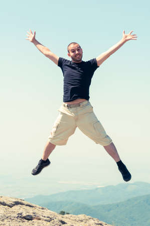 Happy cheerful man jumping on top of the mountain in a summer sunny dayの写真素材