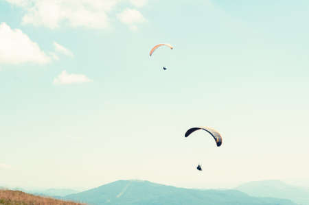 Two paragliders in a blue sky with hills in background on a sunny dayの写真素材