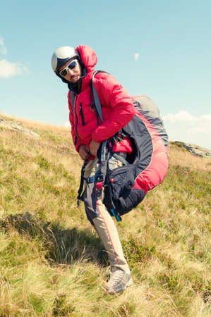 Paraglider wearing equipment ready to take off from a green hillの写真素材