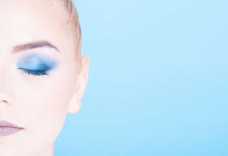 Half face close-up of beauty make-up portrait isolated on blue background with copy text spaceの写真素材
