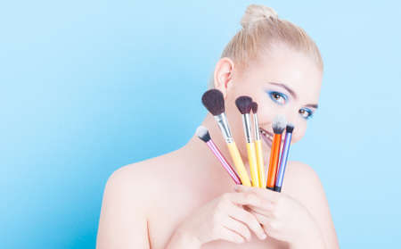 Girl holding make-up professional brushes and smiling or being playful isolated on blue background...