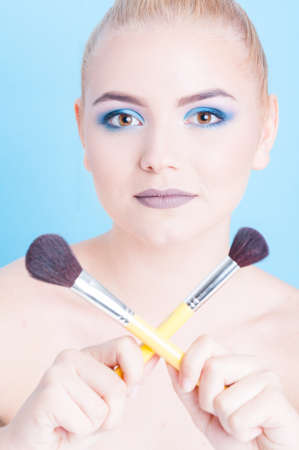 Portrait of girl posing with crossed make-up brushes isolated on blue background