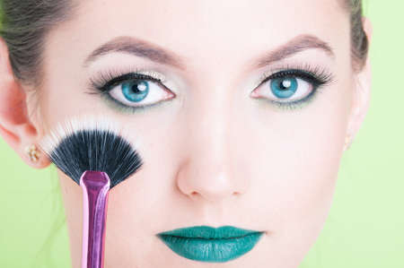 Close-up of woman wearing professional trendy green make-up holding brush isolated on green backgroundの写真素材