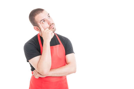 Pensive hypermarket clerk with red apron standing on white background with advertising areaの写真素材