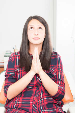 Young lady making praying gesture in dentist chair like being hopefulの写真素材