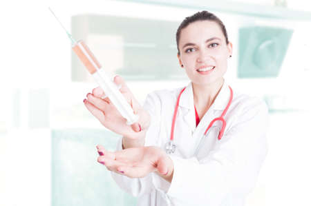 Lady medic showing big syringe and smiling while getting ready for vaccine in her officeの写真素材