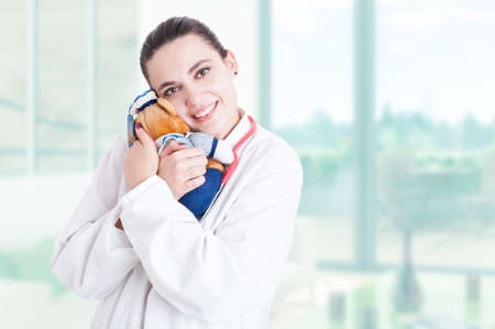 Trustworthy pediatrician with stethoscope and white coat hugging plush toy with advertising areaの写真素材