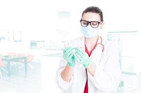 Young medical assistant preparing syringe for injection and wearing protection gloves and mask with text areaの写真素材