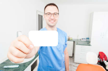 Happy handsome dentist showing business card standing is his cabinetの写真素材