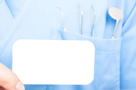 Close-up of dentist holding business card wearing uniform and tools in his pocketの写真素材