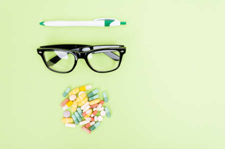 Top view of glasses, capsules and pen isolated on green background with advertising areaの写真素材