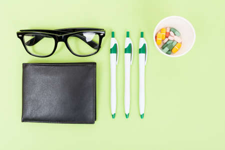 Medical pills, office pencils and black wallet in top view isolated on green backgroundの写真素材