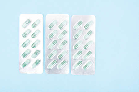 Three blisters full with green capsules isolated on blue background with copy text spaceの写真素材