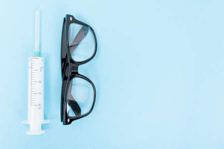 One syringe and pair of glasses on blue background with copy text areaの写真素材