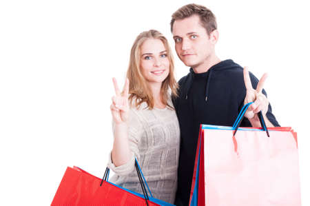 Happy couple holding up bunch of shopping bags making peace gesture isolated on white background...