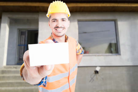 Joyful male builder showing blank visit or business card with advertising area as construction services conceptの写真素材