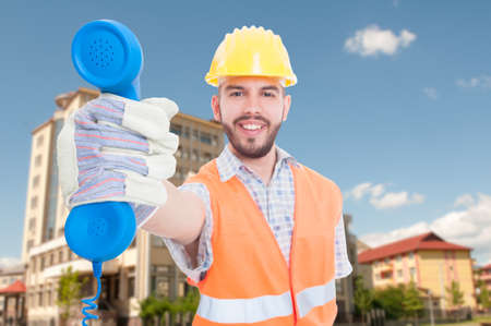 Cheerful young architect giving you the phone receiver as construction business concept
