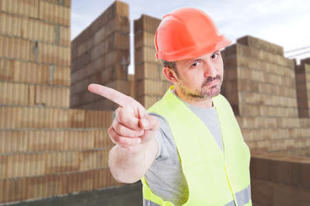 Serious builder in protection equipment doing a refusal gesture while standing on construction siteの写真素材