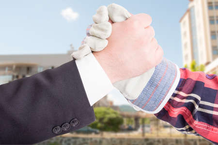 Businessman hand shake with engineer in closeup in front of new buildings after successful meeting