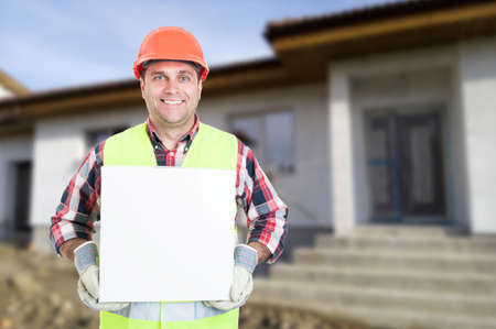 Smiling young builder holding big box on construction site with copy text spaceの写真素材