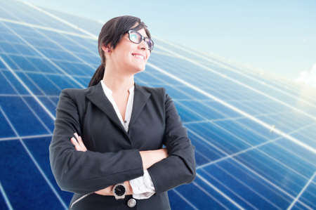 Joyful business woman standing with folded arms looking confident with solar panels behind herの写真素材
