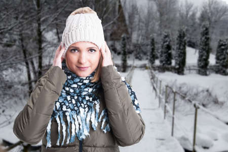 Female model outside in winter park wearing warm jacket, knitted hat and comforter with text space