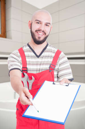 Smiling male plumber giving the clipboard to sign the contract as house reparation conceptの写真素材
