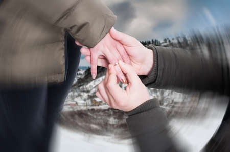 Man putting engagement ring on female hand in winter day as proposal concept with blurred focusの写真素材