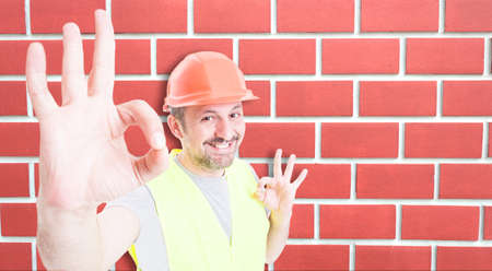 Attractive builder showing double okay sign with happiness on brick wall background with text space