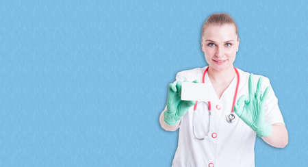 Joyful female medic  showing visit card and doing ok gesture on blue background with copyspaceの写真素材