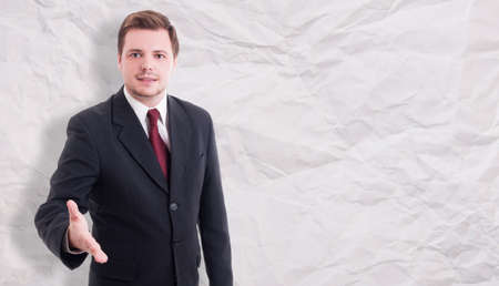 Nice young businessman doing welcoming gesture as partnership concept isolated on wrinkled paper background with copyspaceの写真素材