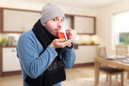 Attractive man is drinking a warm tea to treat his flu indoors as home treatment concept