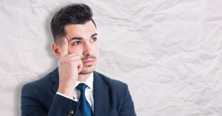 Portrait of pensive young businessman searching for successful solution isolated on wrinkled paper background with advertising areaの写真素材