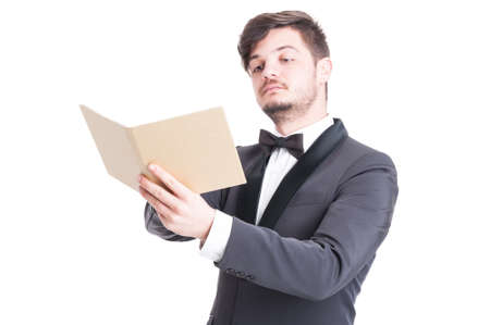 Handsome man wearing tuxedo and bowtie looking at elegant catalogue or agenda isolated on white backgroundの写真素材