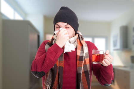 Ill man holding tea cup and blowing his nose in handkerchief as rhinitis conceptの写真素材