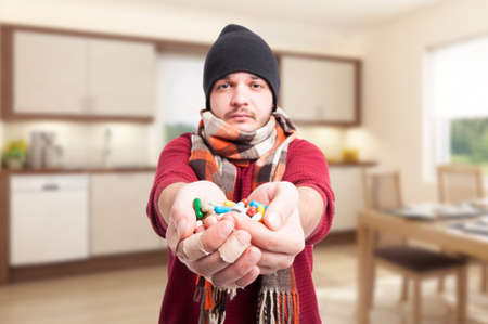 Man with influenza holding pills on his hand and treating his infection inside the houseの写真素材