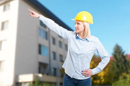 Female engineer wearing yellow helmet pointing something with building on backgroundの写真素材