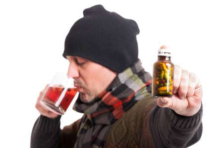 Man with migraine drinking hot tea and holding bottle of pills and capsules on white backgroundの写真素材
