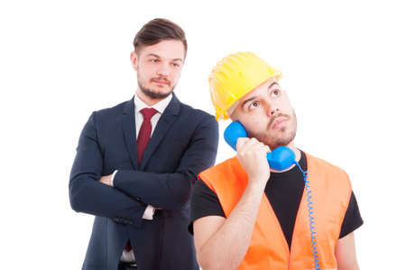 Constructor or engineer calling somebody while businessman standing with folded arms behind him isolated on whiteの写真素材