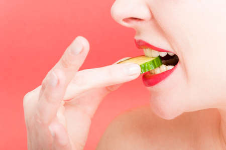 Young woman with slice of cucumber in close-up view isolated on red backgroundの写真素材