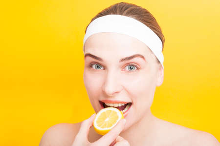 Beautiful girl biting a juicy lemon as fresh diet concept on yellow backgroundの写真素材